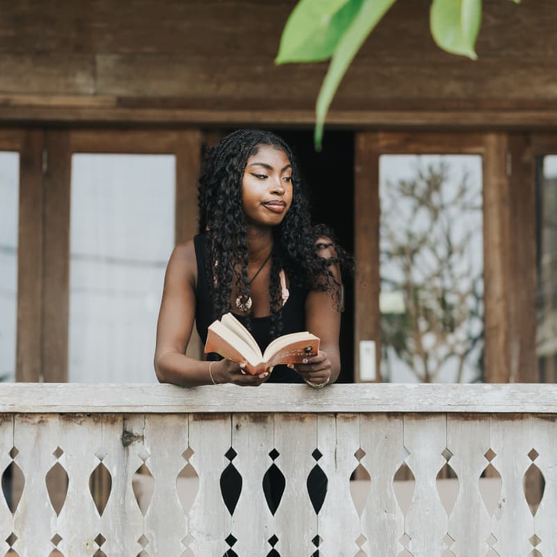 Guest reading book by handcrafted teakwood balcony railing in Canggu Bali joglo villa