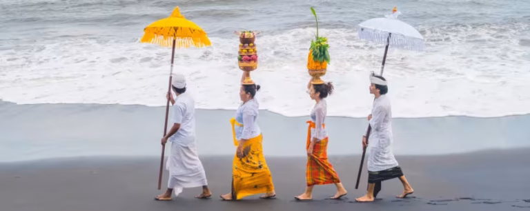 Hindu devotees participating in the Melasti Ceremony, carrying offerings and umbrellas along the beach in Bali, preparing for Nyepi Day.