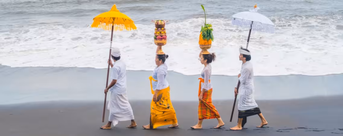 Hindu devotees participating in the Melasti Ceremony, carrying offerings and umbrellas along the beach in Bali, preparing for Nyepi Day.