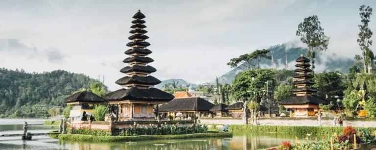 Pura Ulun Danu Bratan, a stunning Balinese temple located by the serene lake with lush greenery and misty mountains in the background, captured at dawn.
