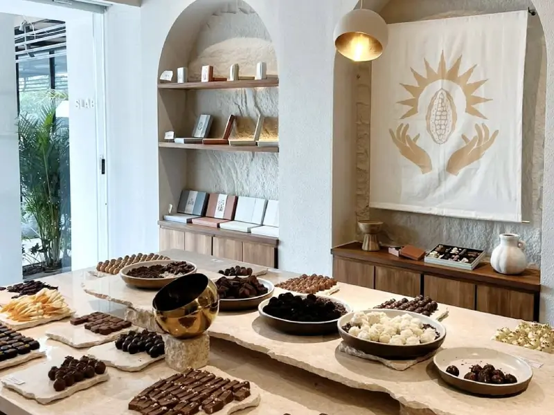 The minimalist and elegant interior of Slab artisan chocolate shop in Canggu, showing a beautiful display of various handmade dark, milk, and white chocolates on a stone counter.