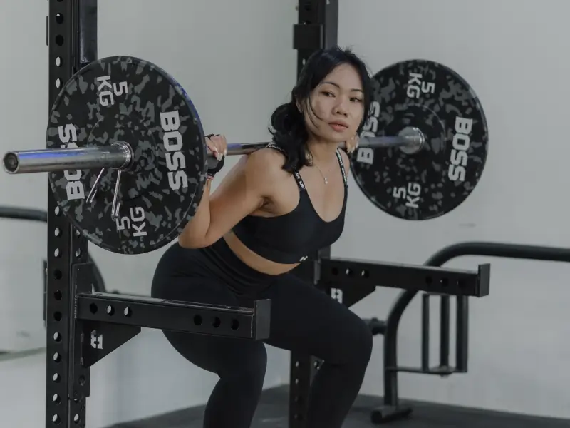 A woman in black athletic wear performing a barbell squat in the modern and well-equipped Avenue Fitness gym in Canggu, with "BOSS" branded weight plates.