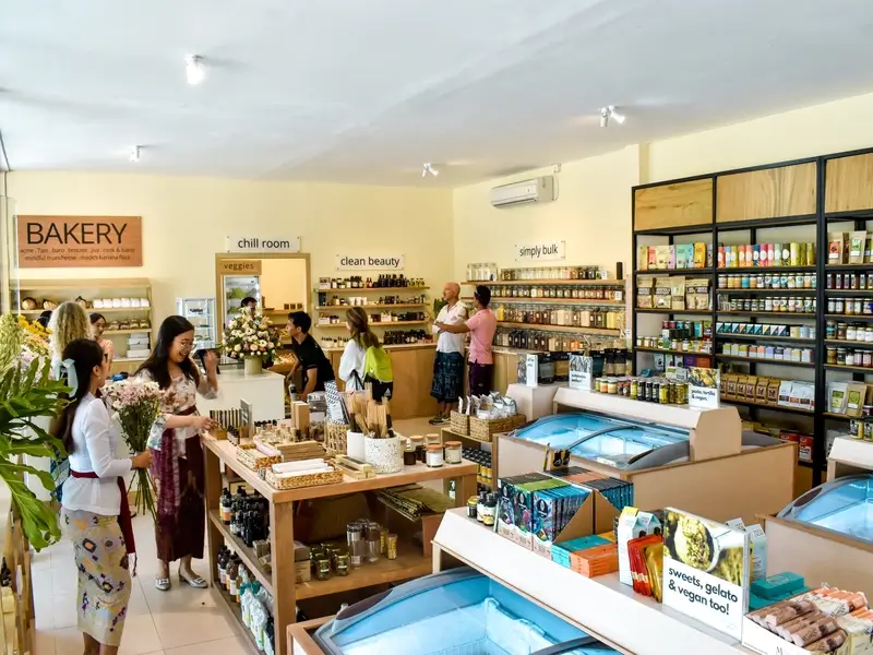 The bright and airy interior of Bali Direct Store in Canggu, with shelves stocked with organic products, a bakery section, bulk foods, and customers shopping for healthy groceries.