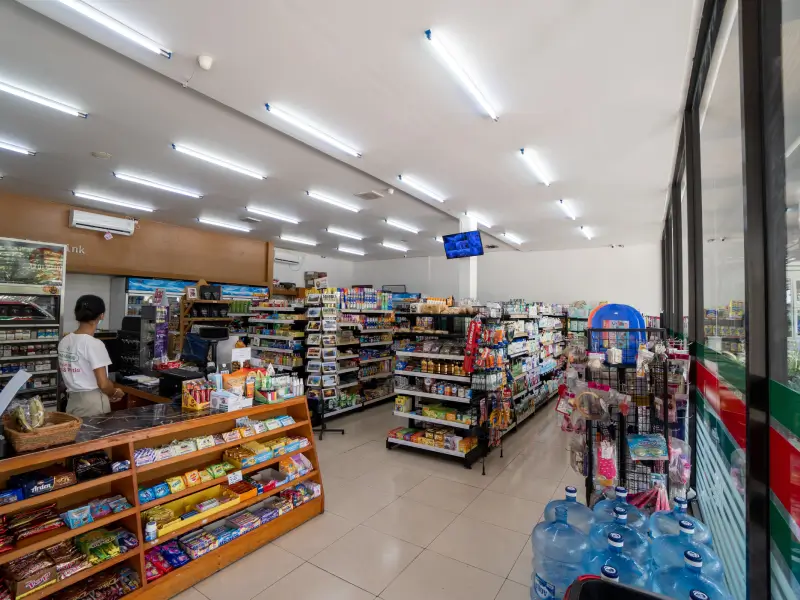 The clean and well-stocked interior of a Dia Mart minimarket in Canggu, showing aisles filled with snacks, drinks, and daily necessities, with a cashier at the counter.