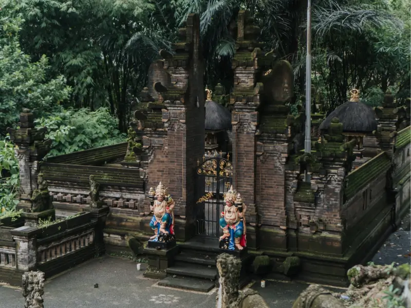 An overhead view of a traditional Balinese temple gate (Candi Bentar) in Canggu, featuring intricate brickwork, stone guardian statues (Dwarapala), and surrounded by dense jungle foliage.