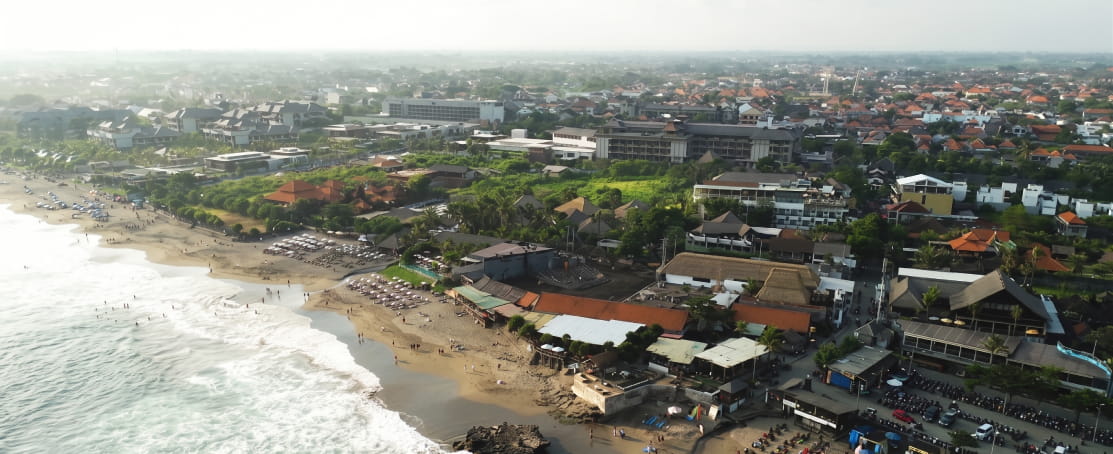 Aerial view of the coastline and town of Canggu, Bali, featuring the sandy beach and ocean waves.